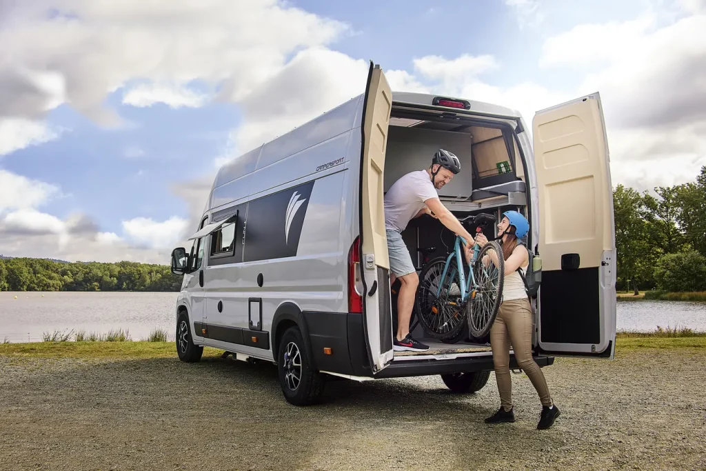 Dreamer Camper Sport con una pareja cargando bicicletas en el garaje trasero, junto a un lago