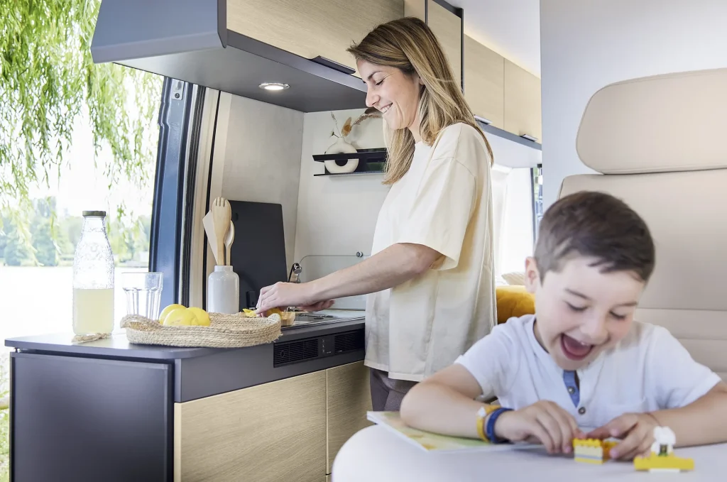 Mujer cocinando y niño jugando en el salón de la camper Dreamer D68